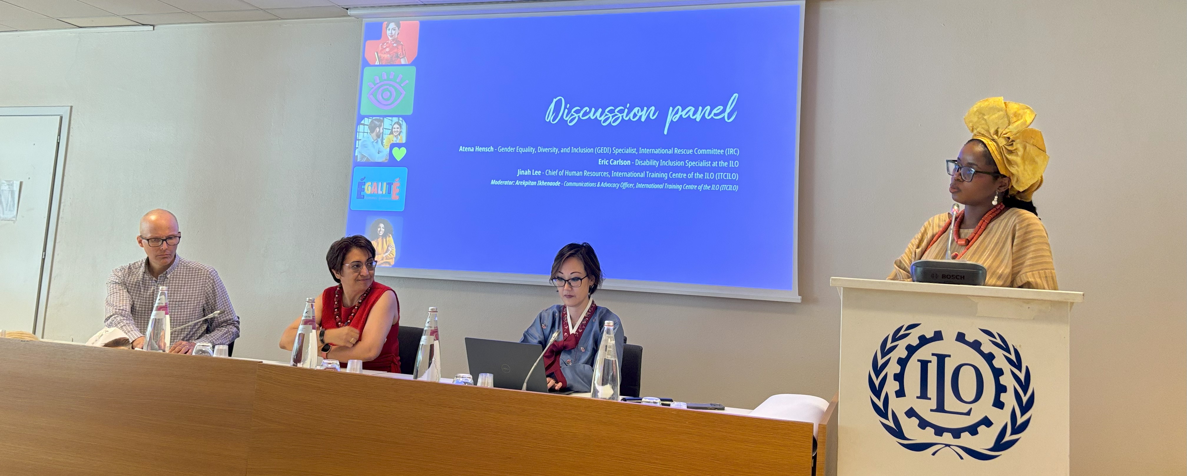Panel discussion with moderator to the right. Panellists are seated and the moderator remains standing. 