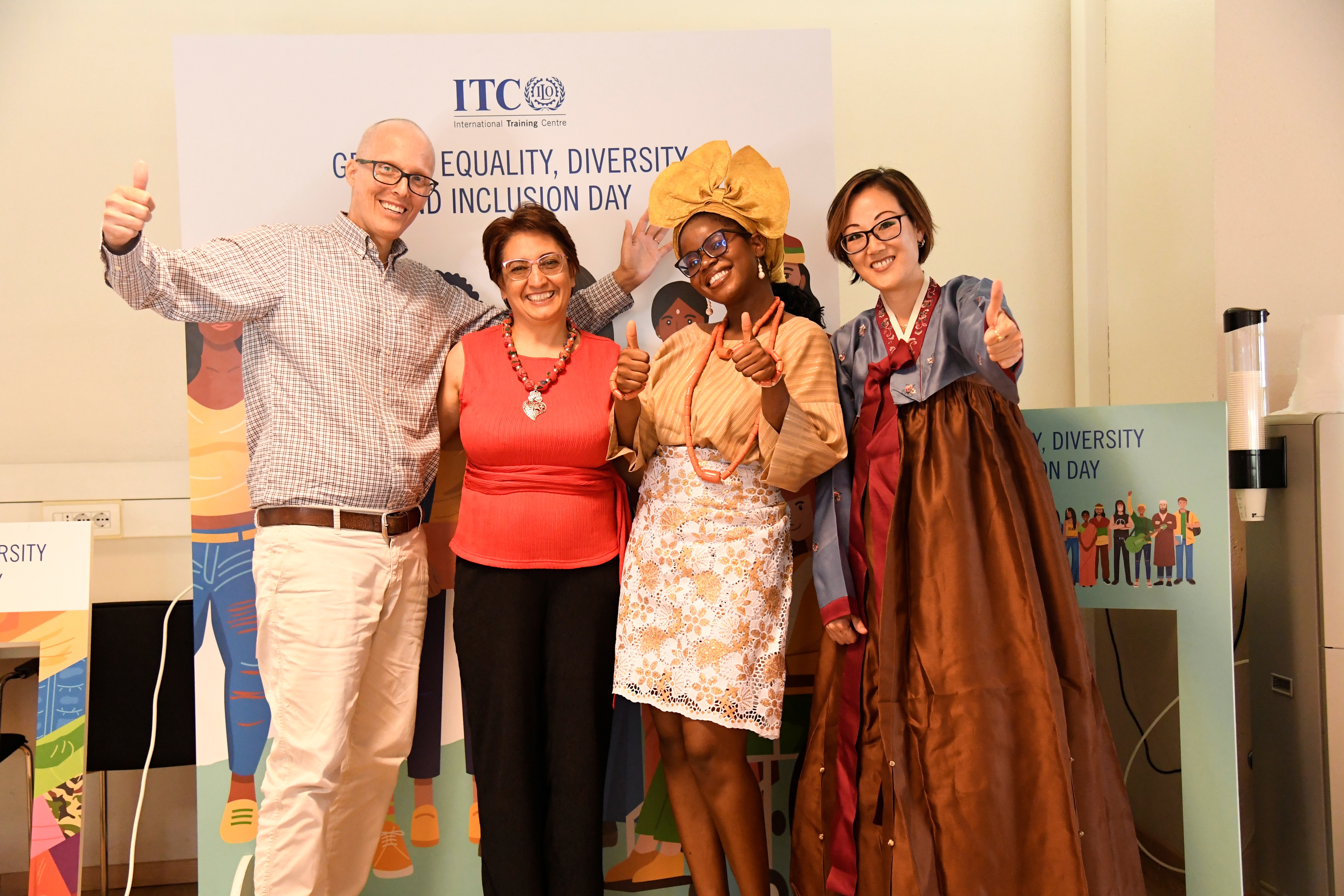 The panellists and moderator smiling and giving thumbs up. Two are dressed in traditional attire and the other two in business casual. 