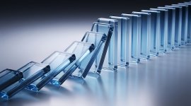 Close-up of transparent blue dominoes falling in sequence, illustrating a chain reaction or cascading effect.