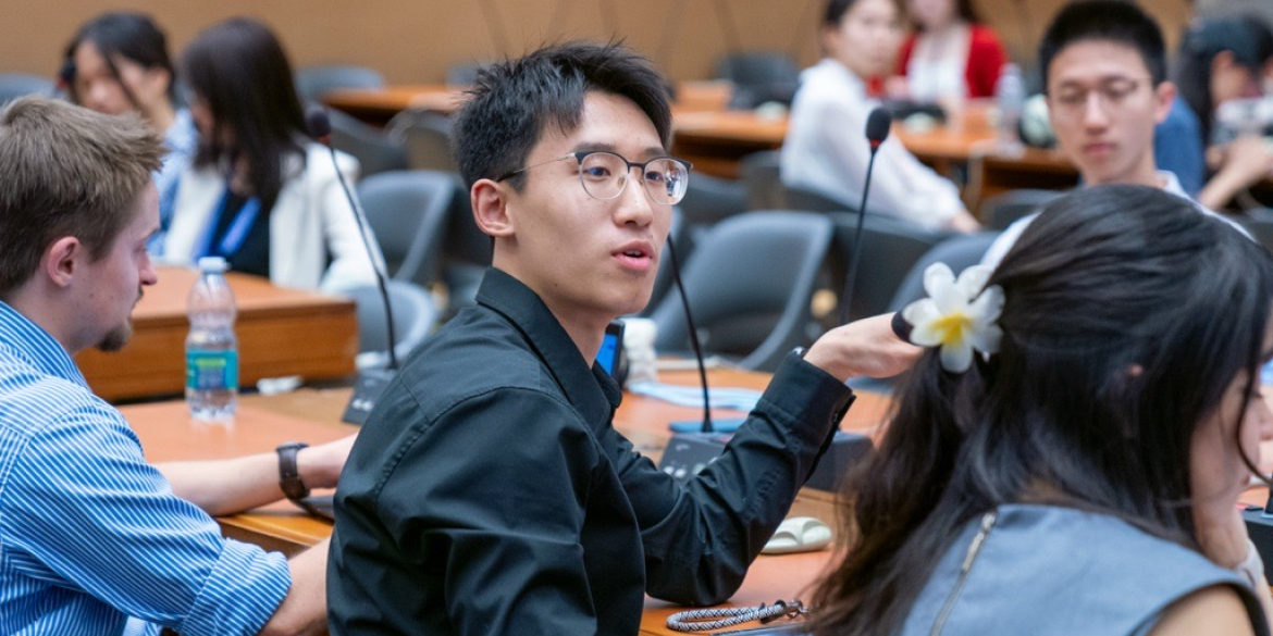Chinese student speaking from a desk in a classroom setting