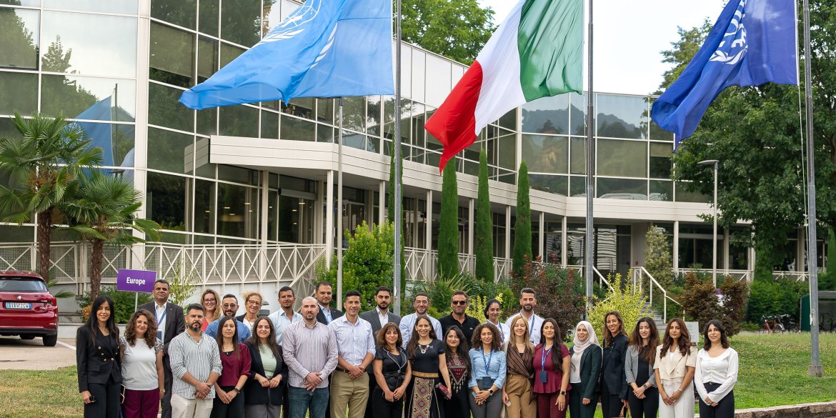 Group photograph taken at the Turin campus in front of the UN, ILO and Italian flags