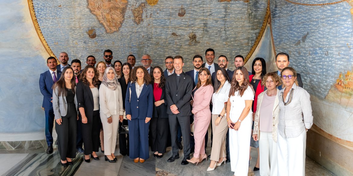 A group of diplomats and officials posing for a photo in front of a large historic world map during an institutional visit.