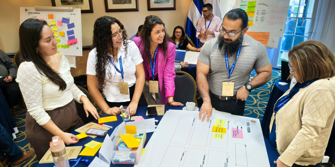 Participants gather around a table covered with notes and colourful cards during an interactive group exercise, discussing ideas and working together.