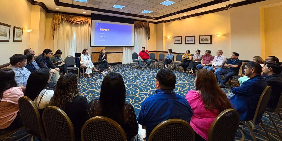 Participants seated in a large circle during a facilitated workshop session, listening to a presentation and engaging in group discussion.