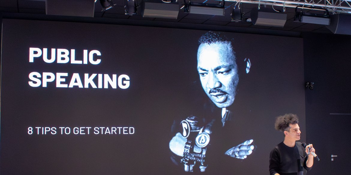 A facilitator presents eight tips for public speaking in front of a large screen featuring Martin Luther King Jr.