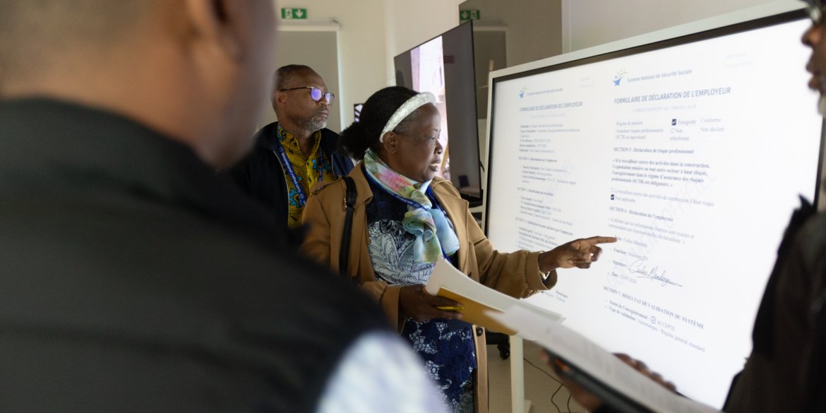  A woman points to information on a digital screen during a group discussion, while other participants look on.