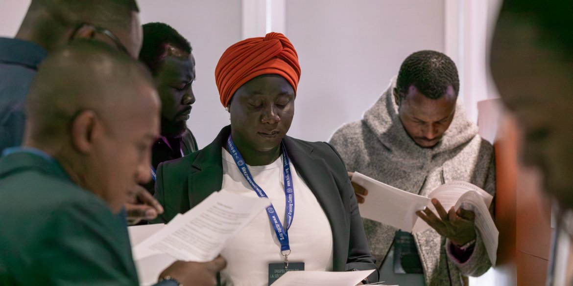 Participants review printed documents together during a group activity, with a woman in an orange headwrap at the centre.