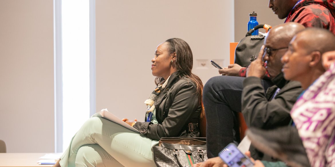 Participants sit together during a session, with a woman holding notes and listening attentively.
