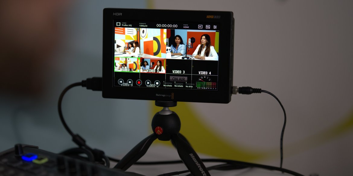 A close-up of a video production monitor in the ITCILO Media Lab, displaying multiple camera angles of two women speaking into microphones against a colourful geometric backdrop.