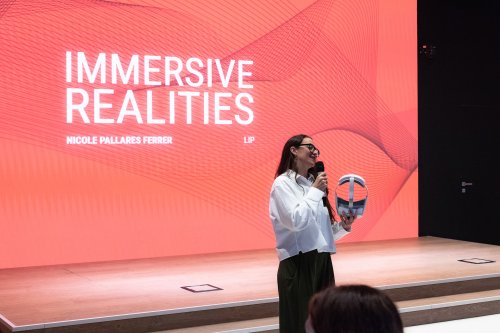 Nicole Pallares Ferrer, ITCILO Extended Reality Specialist, demonstrates immersive technologies on stage during Innovation Day 2026, against a large red screen displaying “Immersive Realities.”
