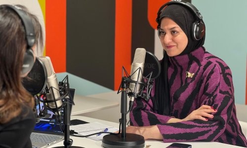 woman in a podcasting studio with headphones and a microphone
