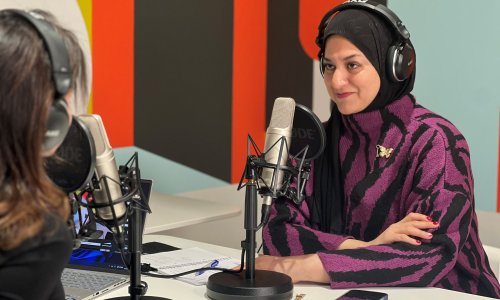 Two women wearing headphones speak into microphones during a podcast recording.
