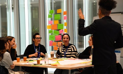 Participants engage in an interactive group discussion during a workshop, surrounded by colourful sticky notes and materials.