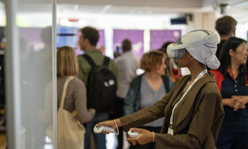 A participant wearing headphones sits during a neurotechnology demonstration at the ITCILO AI+ Nonference, while other attendees observe and interact in the background.