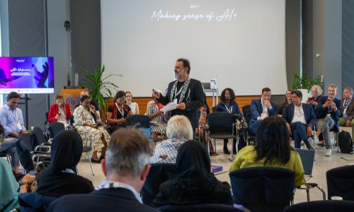 A speaker addresses a seated audience during the ITCILO AI+ Nonference, with presentation screens visible at the front of the conference hall.