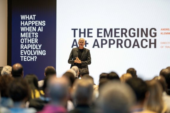 A speaker addresses a seated audience at the ITCILO AI+ conference, standing in front of a large presentation screen displaying “The Emerging AI+ Approach” and a question about AI's intersection with other rapidly evolving technologies.